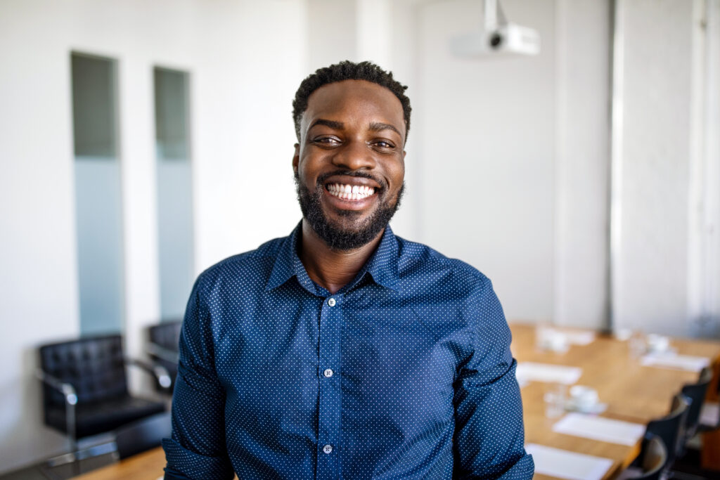 Portrait of a smiling young businessman Portrait of a smiling young businessman standing in office. Cheerful african man at work, standing in startup office board room.