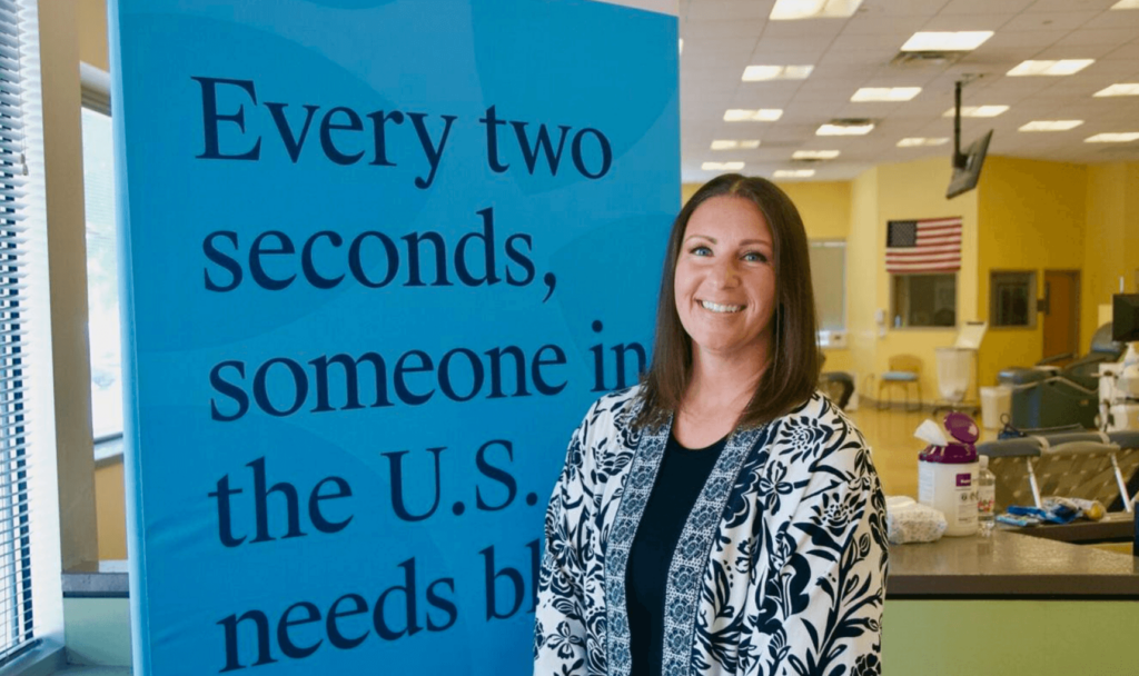 Blood Donor Angela P. featured smiling in front of a Banner at Inova